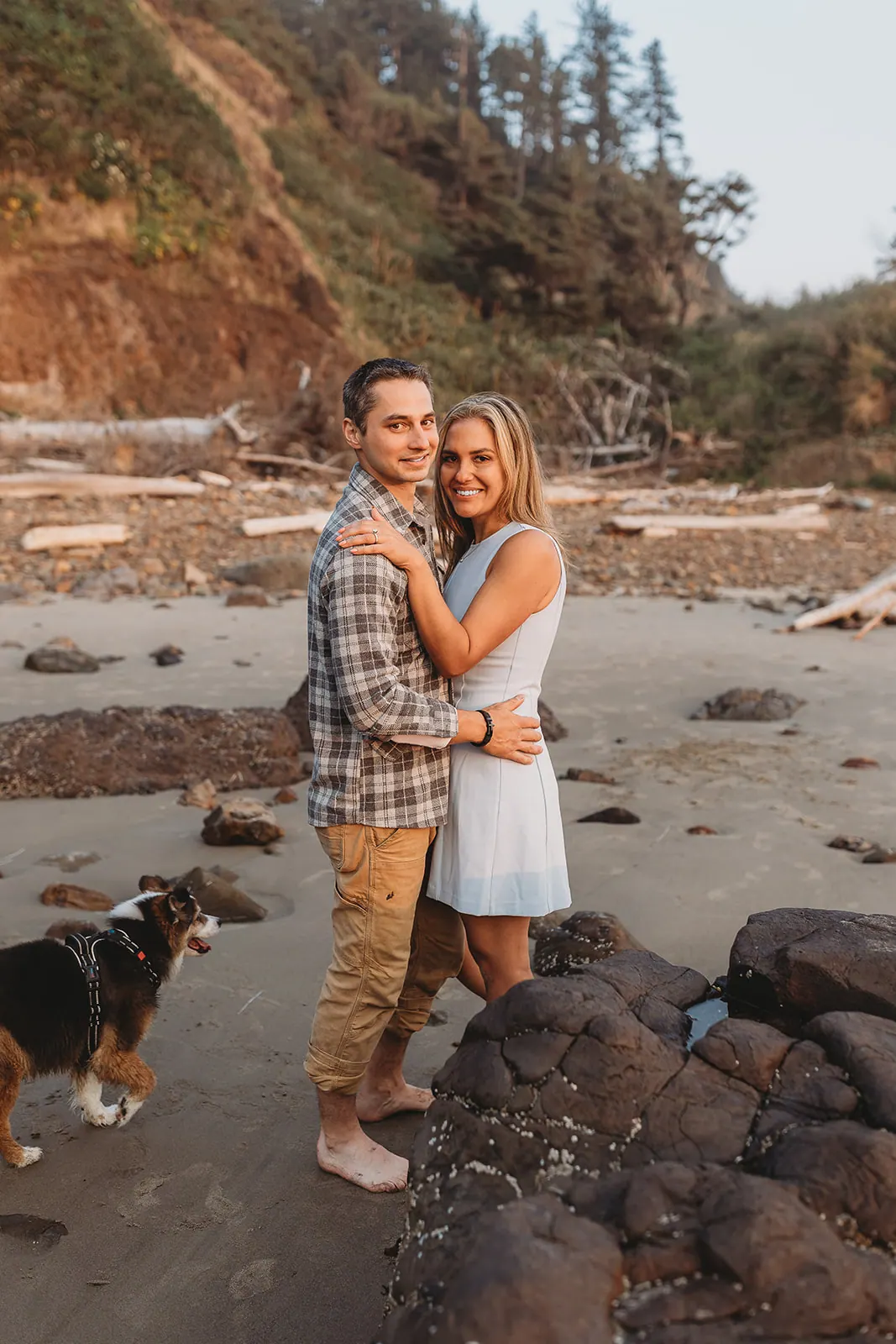 Olivia and her fiancé with a dog on a rocky beach